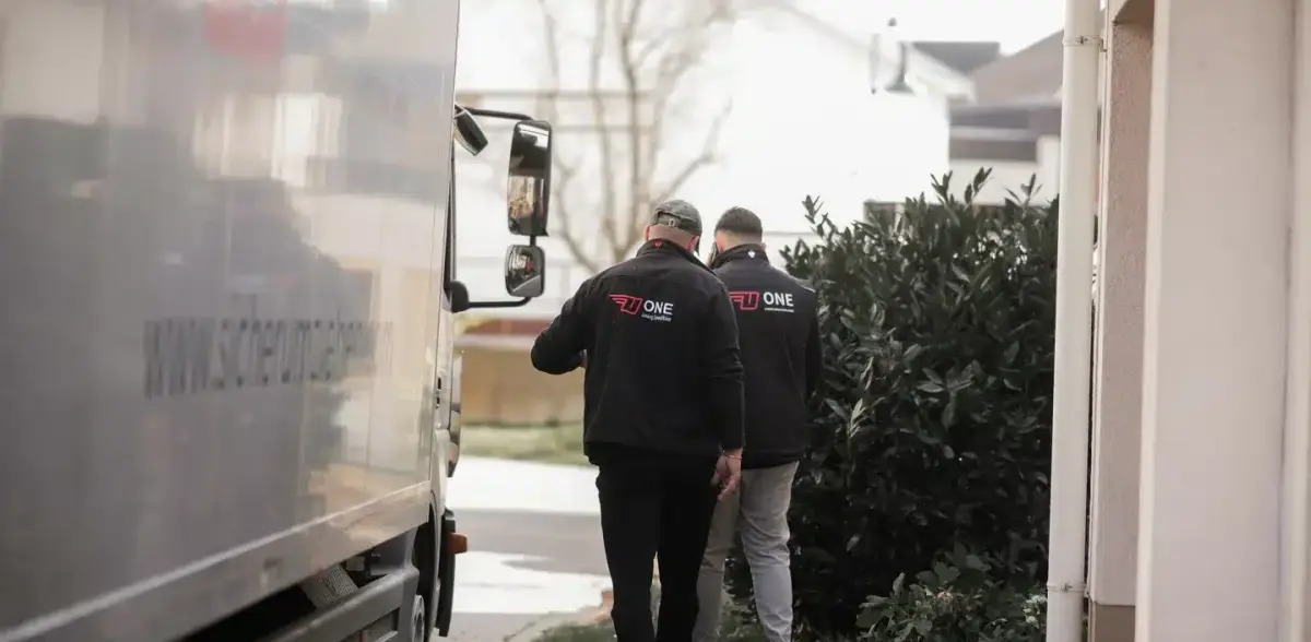 Zwei Mitarbeiter in ONE-Jacken gehen vom Möbelwagen aus auf den Hauseingang zu.