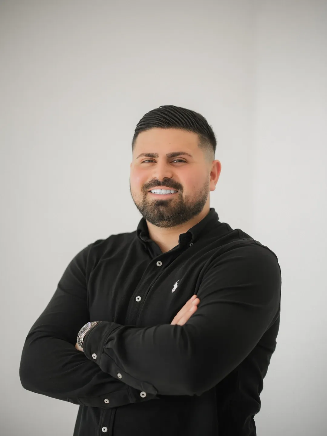 Porträt von Ugur Kosar im schwarzen Hemd, mit verschränkten Armen vor einer hellen Wand.