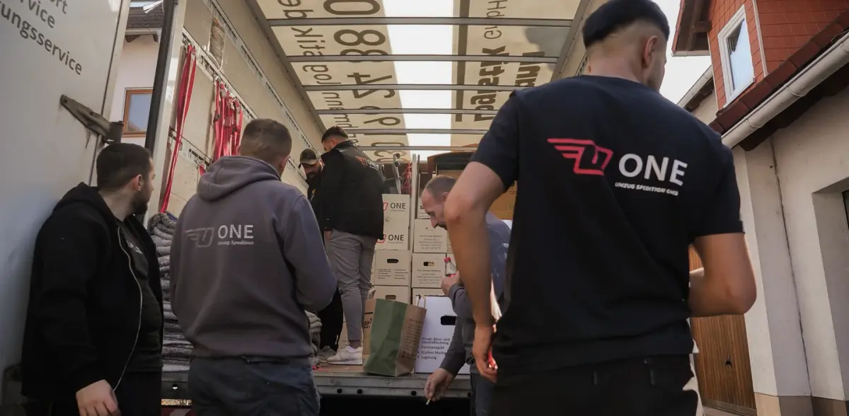 Mehrere Mitarbeiter in ONE-Shirts stapeln beschriftete Umzugskartons im offenen Möbelwagen.