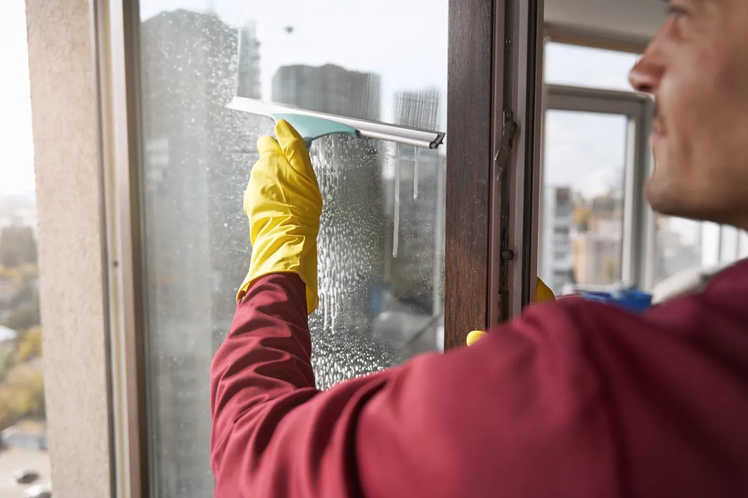 Person mit gelbem Gummihandschuh zieht eine eingeschäumte Fensterscheibe mit dem Abzieher ab.