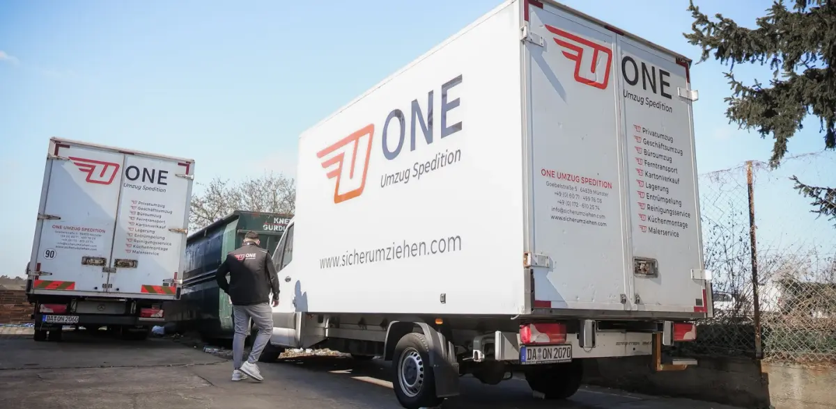 Zwei Möbelwagen der One Umzugsspedition auf dem Betriebshof, ein Mitarbeiter steigt in die Fahrerkabine.