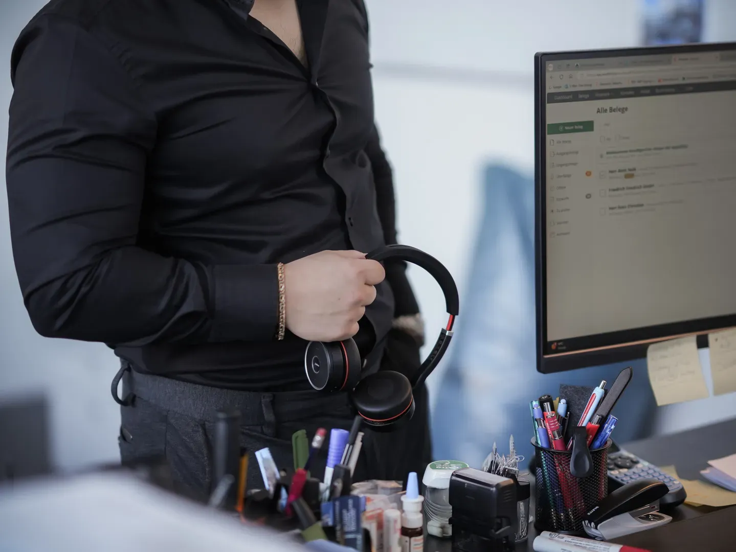 Mitarbeiter im schwarzen Hemd hält am Schreibtisch ein Headset in der Hand.