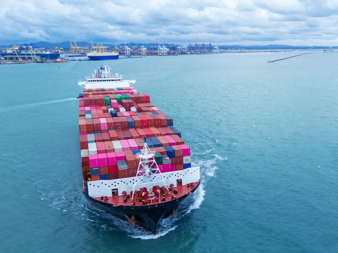 Containerschiff läuft auf einen Hafen mit Verladekränen zu.