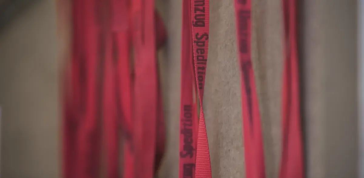 Rote Spanngurte mit der Aufschrift One Umzug Spedition hängen neben Packdecken an der Laderaumwand.