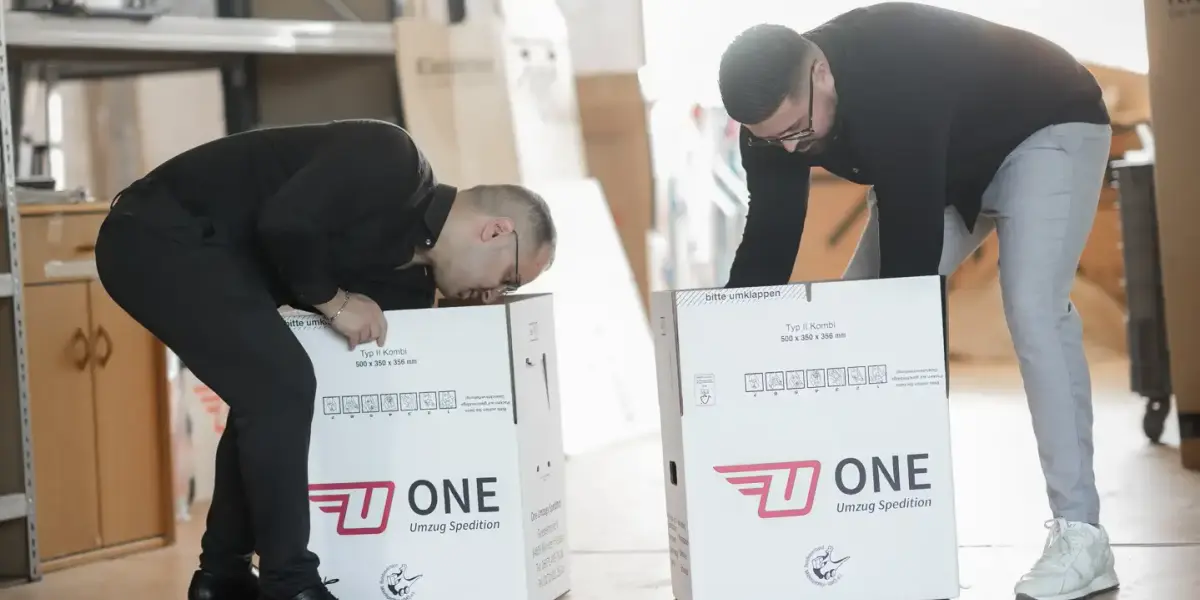 Zwei Mitarbeiter falten im Lager neue ONE-Umzugskartons für den nächsten Auftrag auf.
