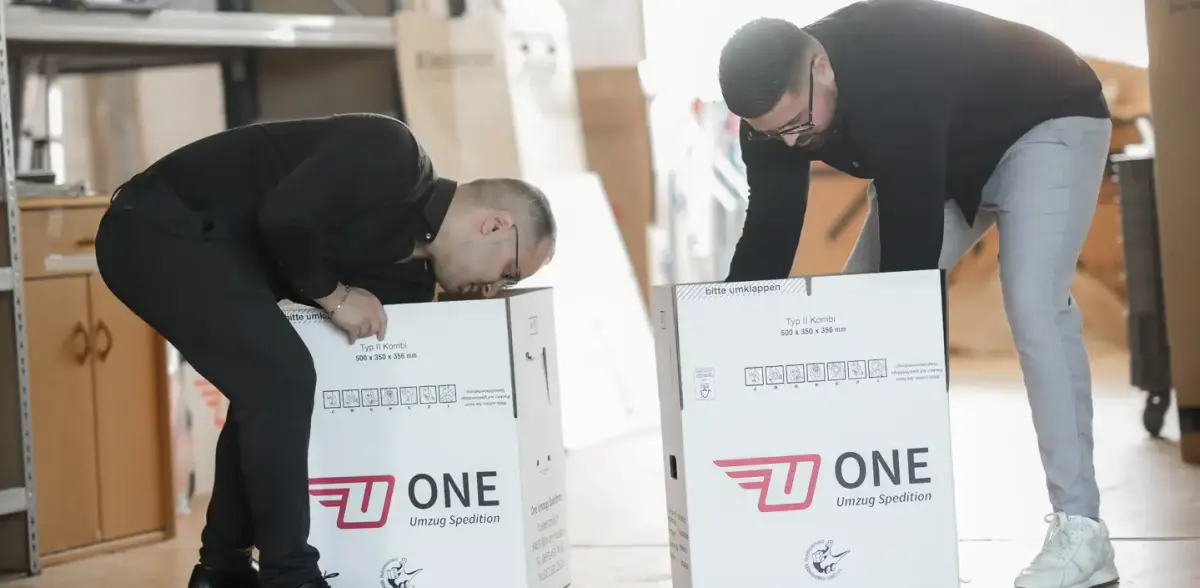 Zwei Mitarbeiter falten im Lager neue ONE-Umzugskartons für den nächsten Auftrag auf.