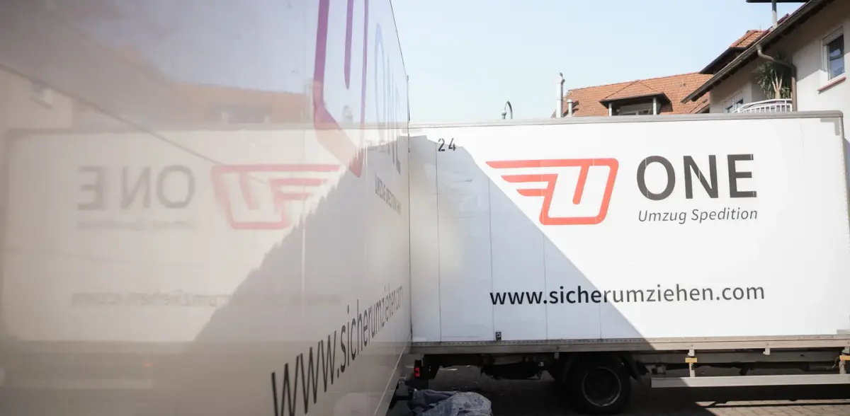 Zwei Möbelwagen mit ONE-Schriftzug stehen dicht nebeneinander vor einem Wohnhaus.