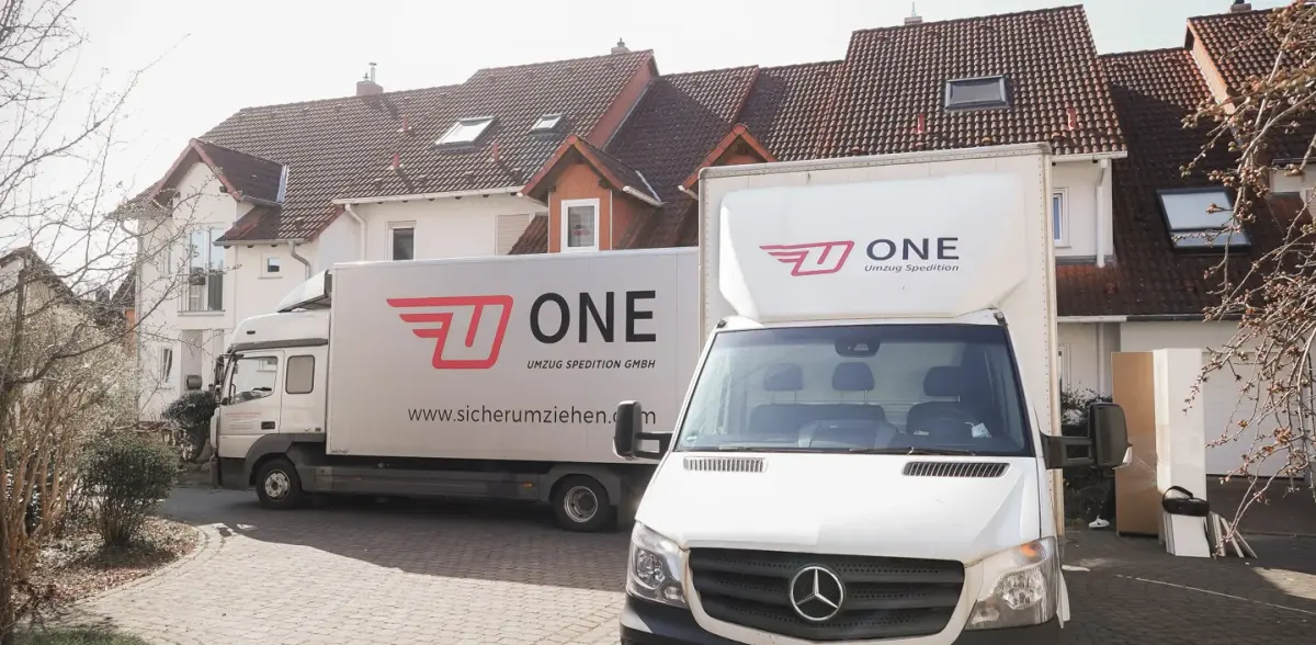 Möbelwagen und Transporter der One Umzugsspedition stehen während eines Einsatzes in einer Wohnstraße.