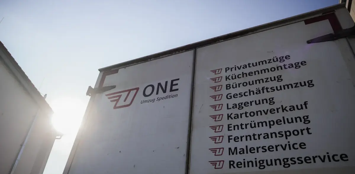 Geöffnete Hecktür eines weißen ONE-Möbelwagens: links das rote Firmenzeichen mit Schriftzug, rechts die Leistungsliste von Privatumzüge bis Reinigungsservice, jede Zeile mit dem roten Zeichen davor.
