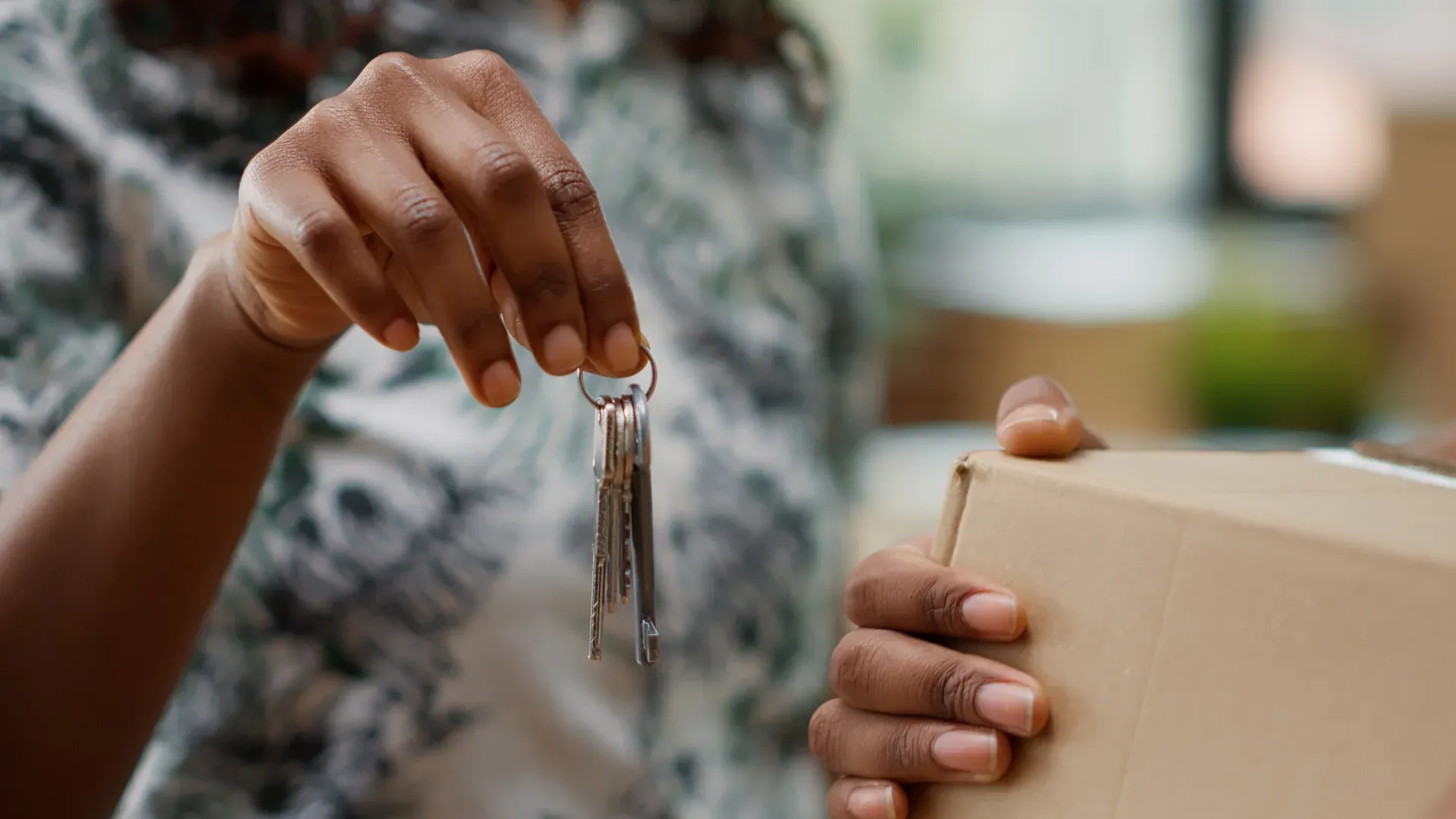 Frau hält in einer Hand einen Wohnungsschlüsselbund und trägt in der anderen einen Umzugskarton
