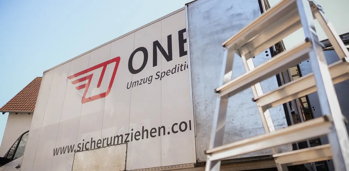 Möbelwagen mit ONE-Logo und Webadresse vor einem Wohnhaus, rechts eine Alu-Leiter vor der geöffneten Hecktür.