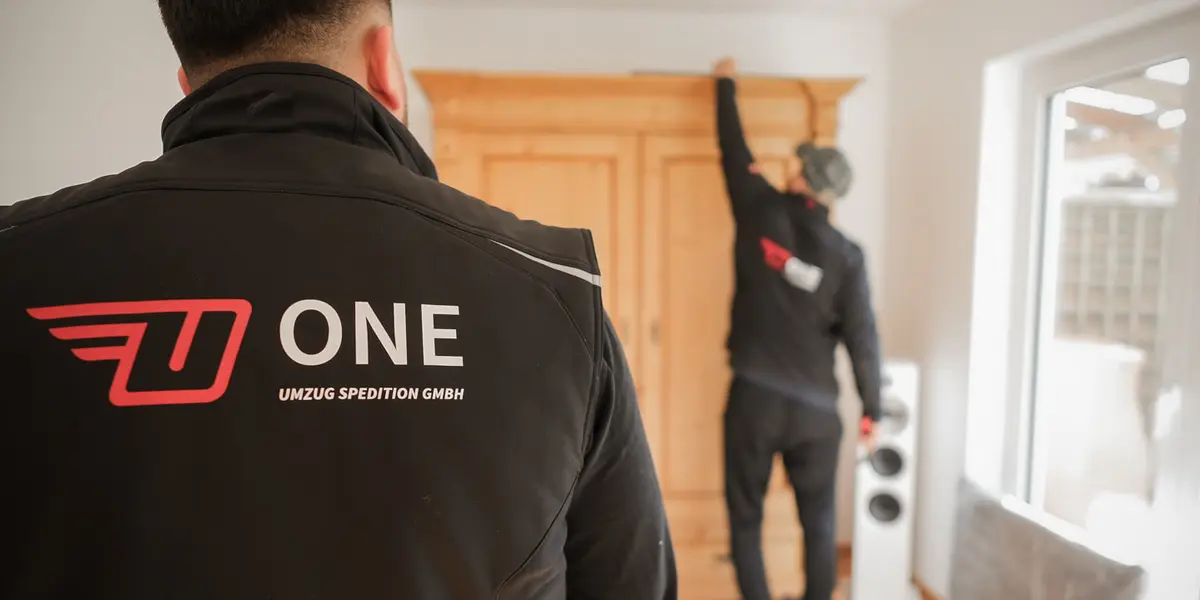 Mitarbeiter mit ONE-Logo auf dem Rücken, im Hintergrund arbeitet ein Kollege in einer Wohnung an einem Holzschrank.