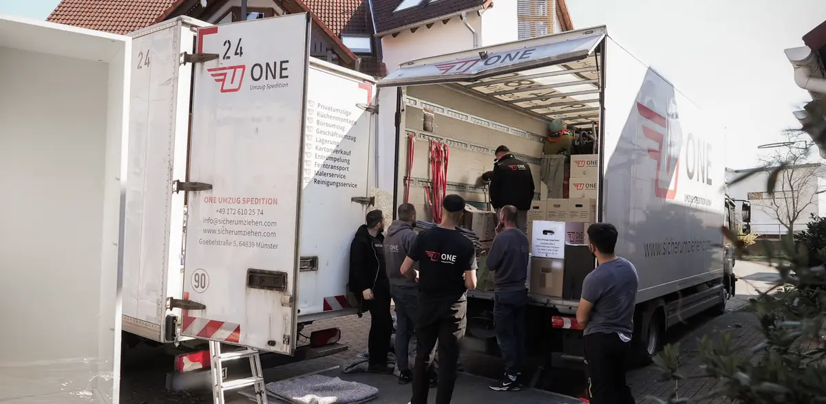 Umzugsteam in ONE-Kleidung an den geöffneten Hecktüren zweier ONE-Möbelwagen vor einem Wohnhaus.