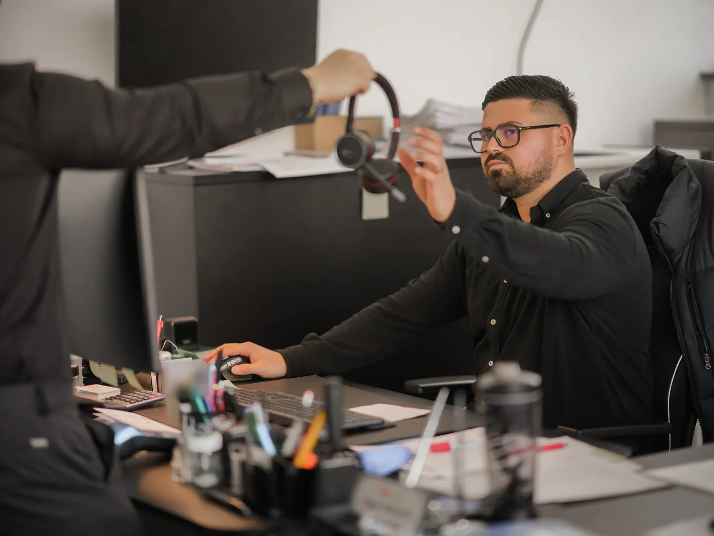 Mitarbeiter der One Umzugsspedition am Schreibtisch, ein Kollege reicht ihm ein Headset.