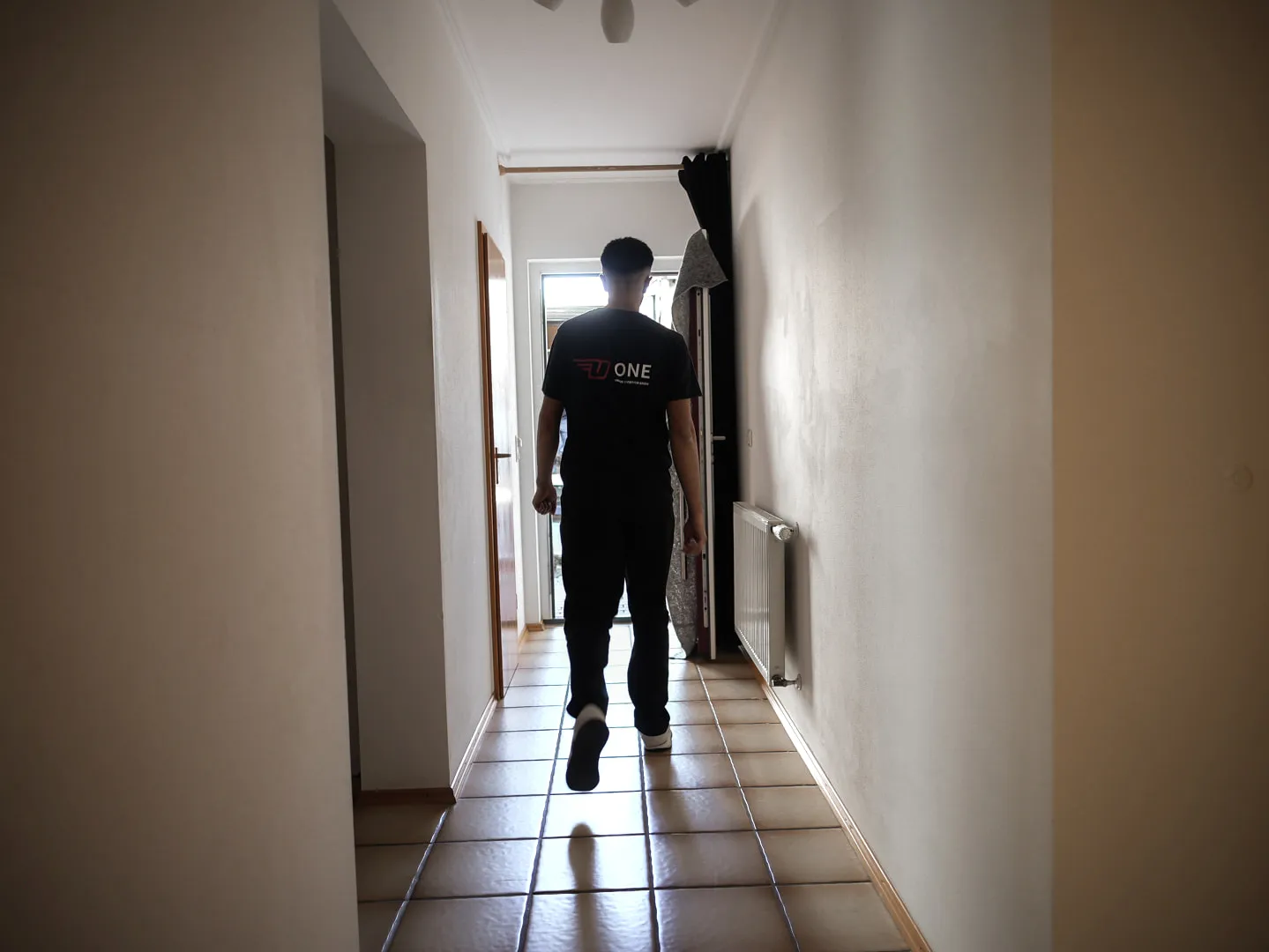 Mitarbeiter im ONE-T-Shirt geht durch einen leeren, gefliesten Flur zur offenen Tür.