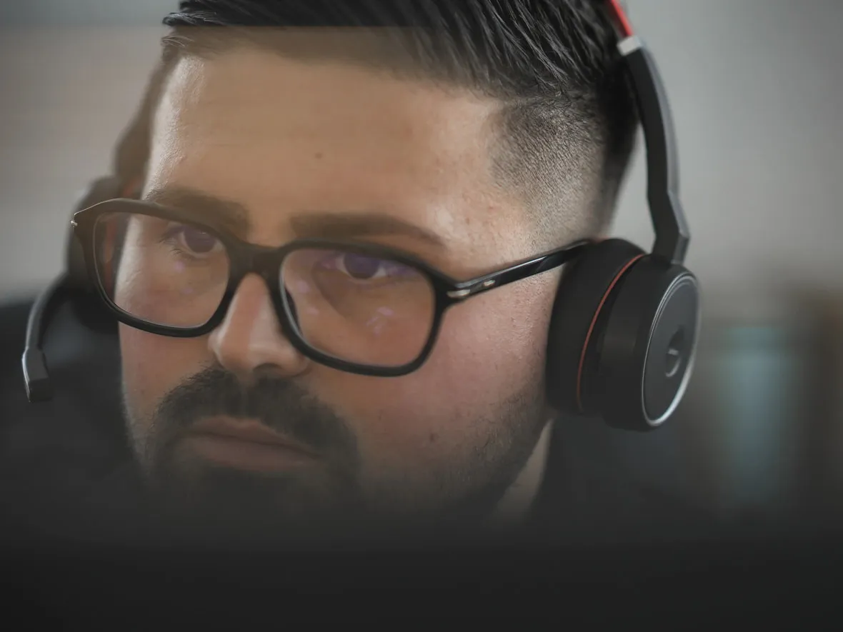 Mitarbeiter mit Brille und Headset blickt konzentriert nach vorn, im Vordergrund unscharf der Bildschirmrand.