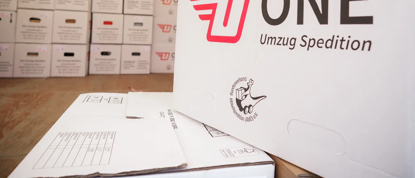 Umzugskarton der One Umzugsspedition mit dem Verbandszeichen der AMÖ.