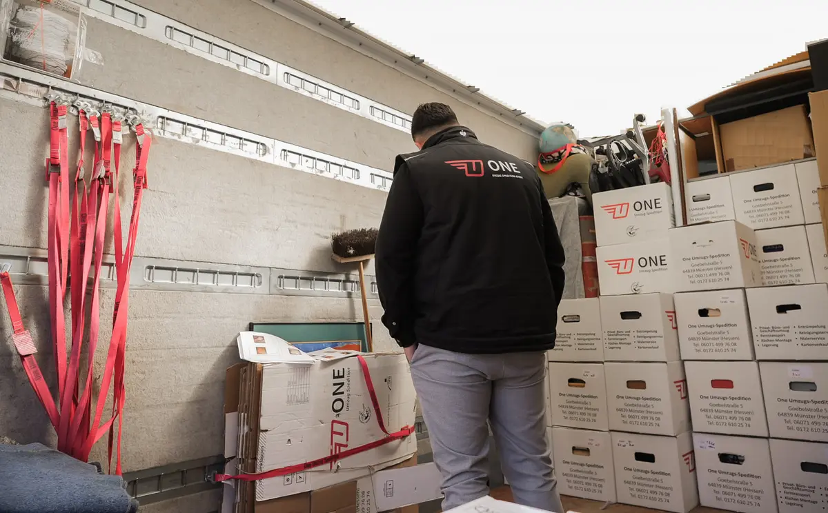 Mitarbeiter in schwarzer ONE-Weste steht im Laderaum des Möbelwagens vor einer Wand aus ONE-Umzugskartons.