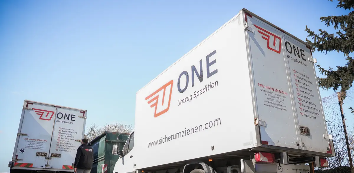 Zwei Möbelwagen mit ONE-Logo und Webadresse stehen auf dem Betriebshof.