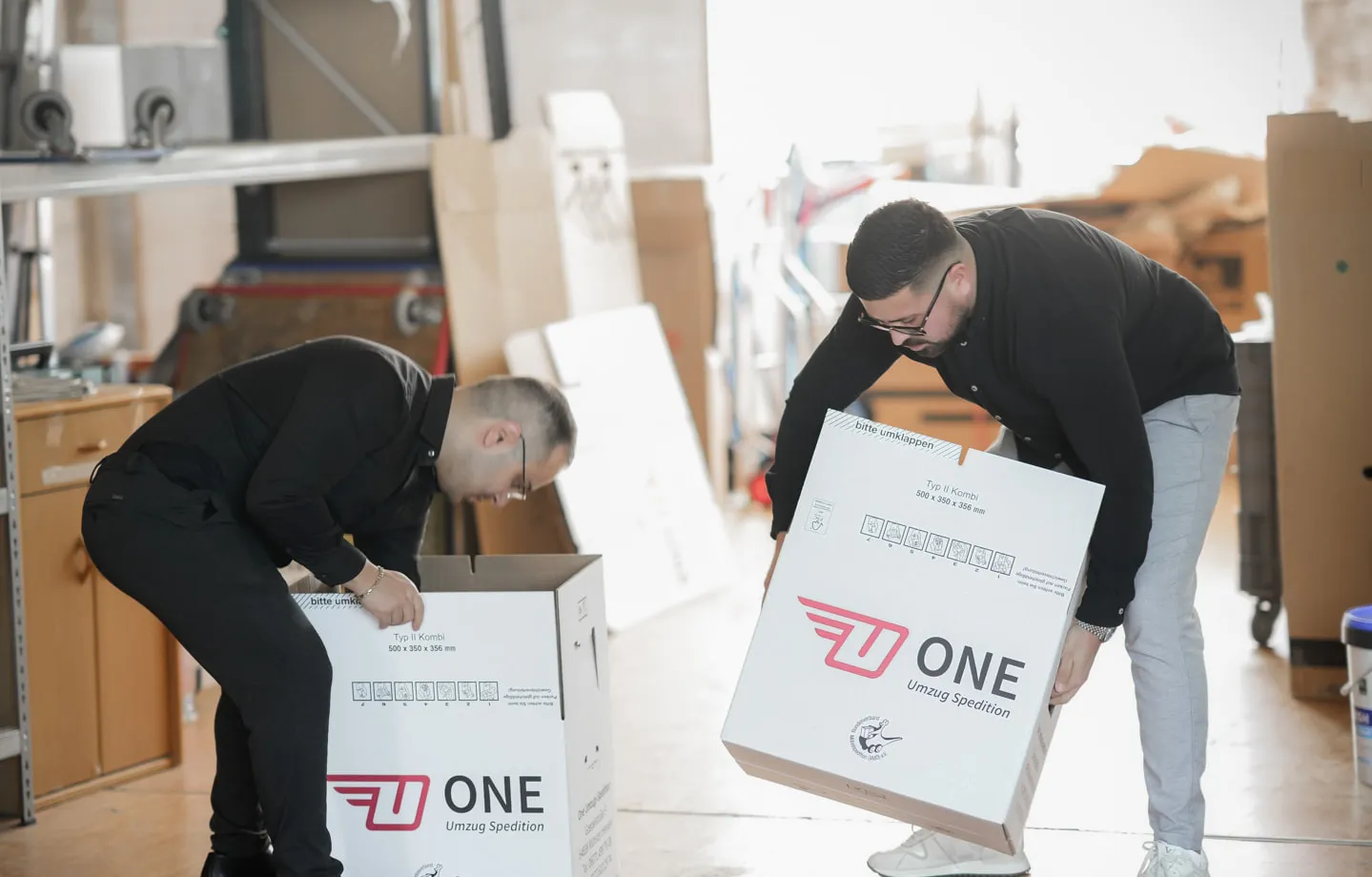 Zwei Mitarbeiter von ONE falten im Lager Umzugskartons mit ONE-Logo auf